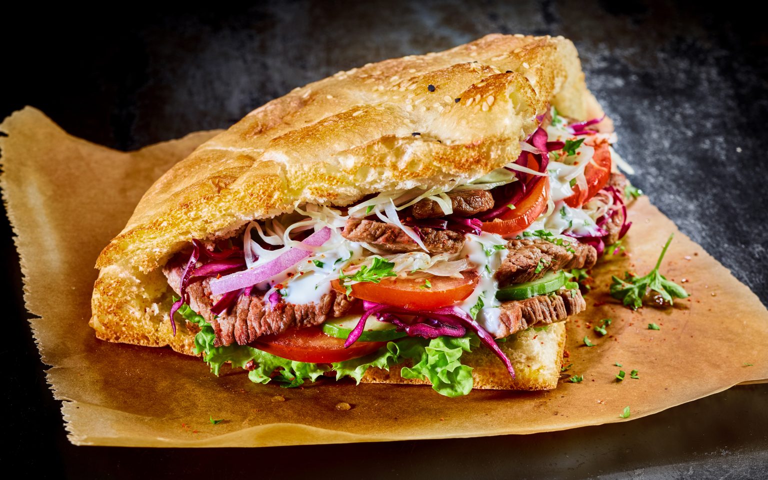 Turkish doner kebab on golden toasted pita bread filled with rotisserie roasted meat and fresh salad ingredients served on brown paper